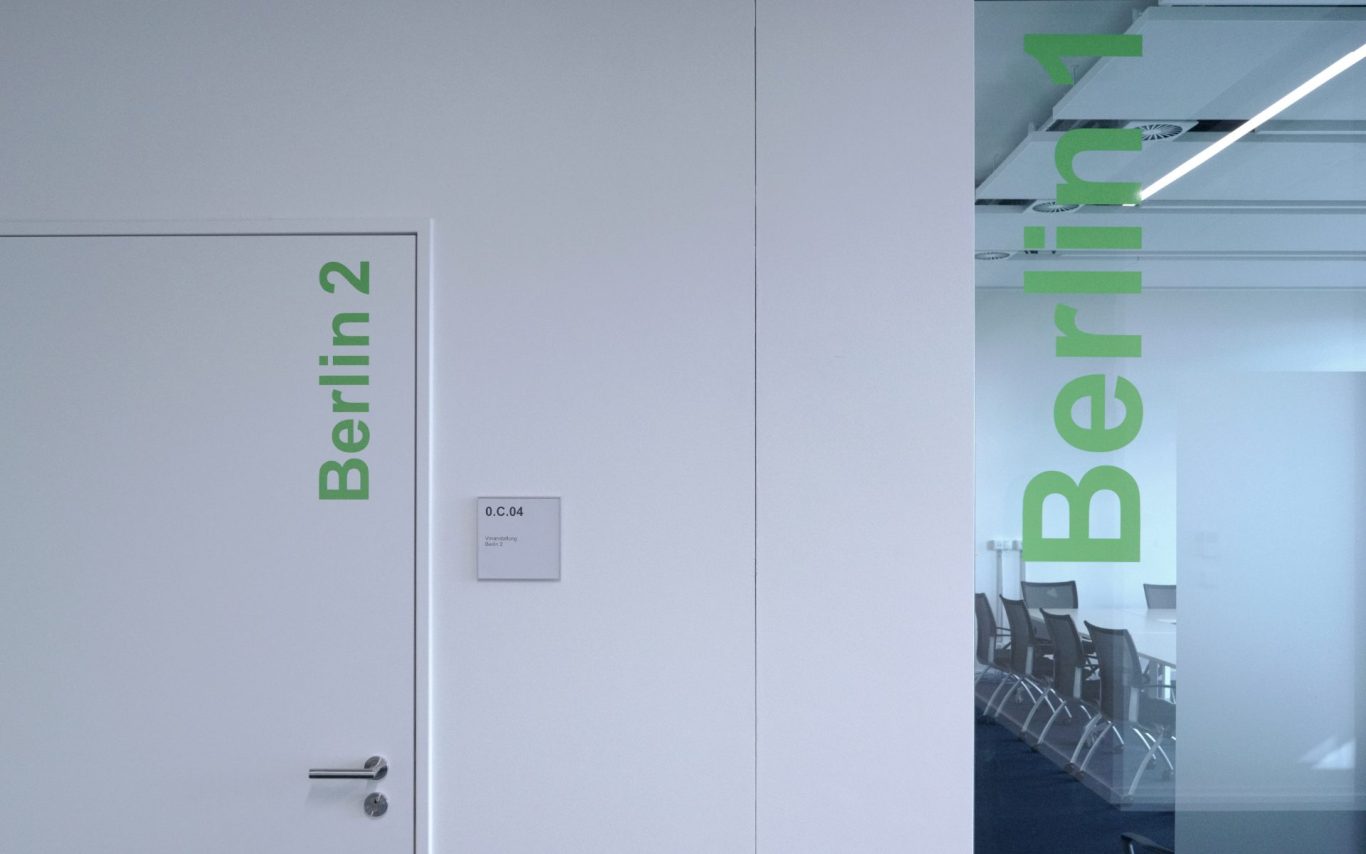 Tür mit Beschriftung "Berlin 2" und Glaswand mit "Berlin 1" in grünem Text.
