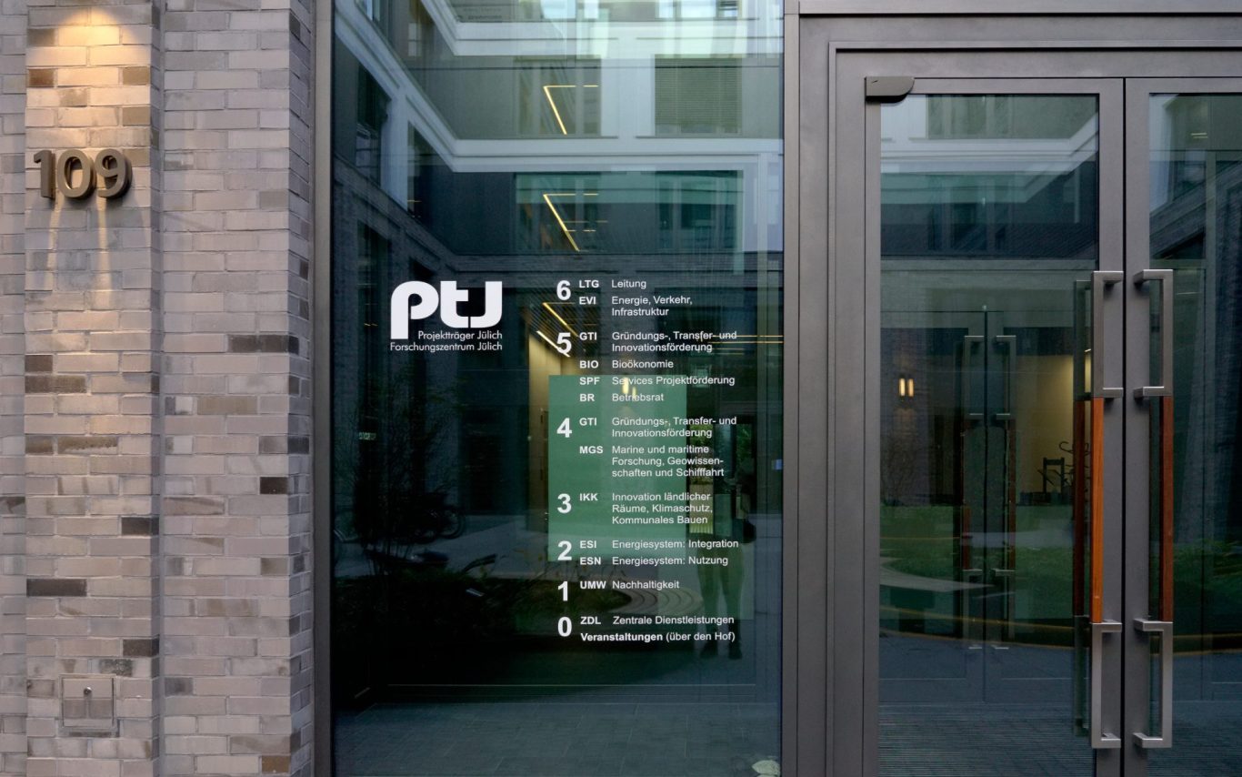 Gebäudeeingang mit Glasfront, Hausnummer, Etagenzahlen und Mieterbeschriftung.