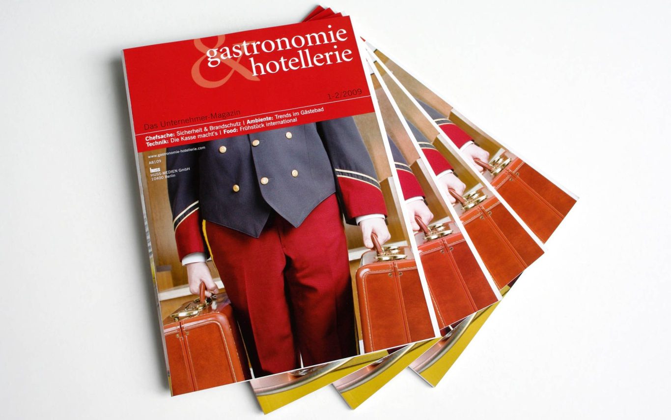 Ein Stapel Zeitschriften mit rotem Cover und einem Portier im Hintergrund.