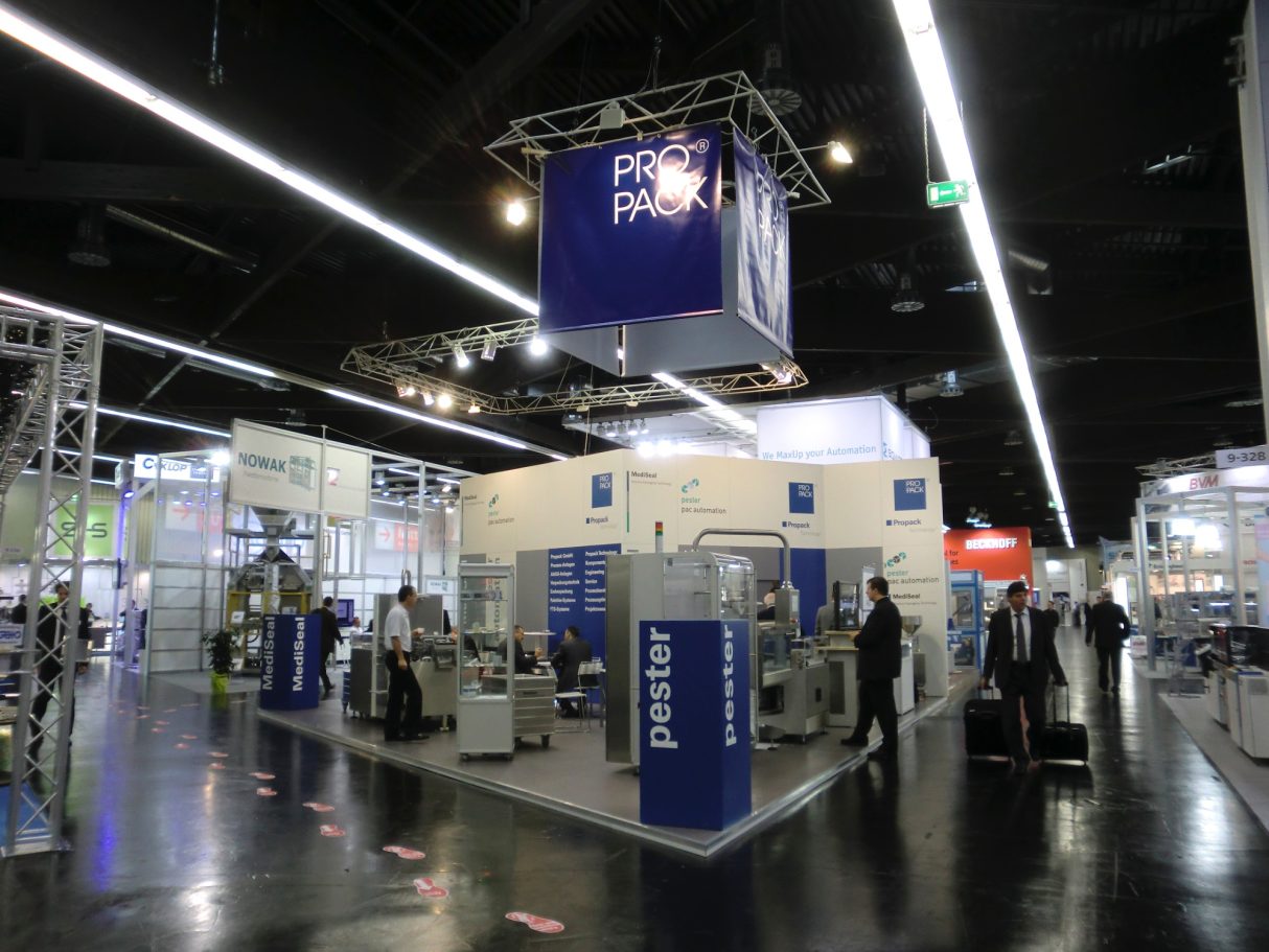 Messestand mit modernen Geräten und Ausstellern in einer großen, hellen Halle.