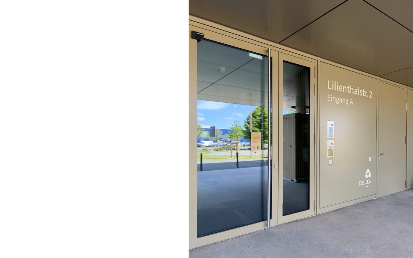 Gestaltung Eingangsbeschriftung Hausadresse und Hausnummer Bürohaus Schönefeld Eingang eines modernen Gebäudes mit Glastür und beigener Eingangsbeschriftung