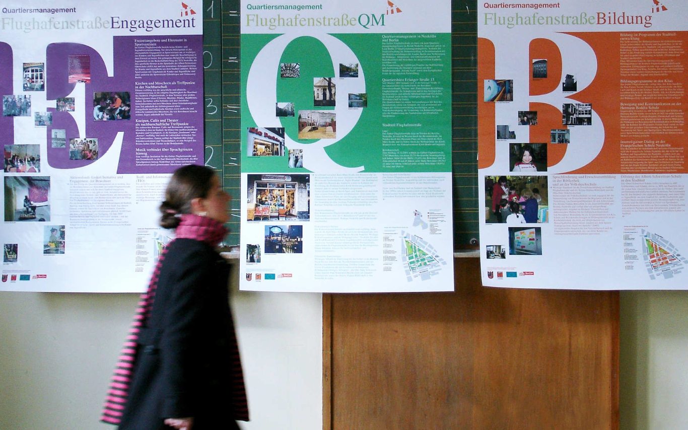 Eine Person steht vor Informationsplakaten in lila, grün und orange.