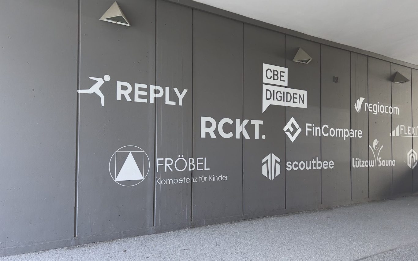 Wand mit Logos verschiedener Unternehmen in grauer Farbe.