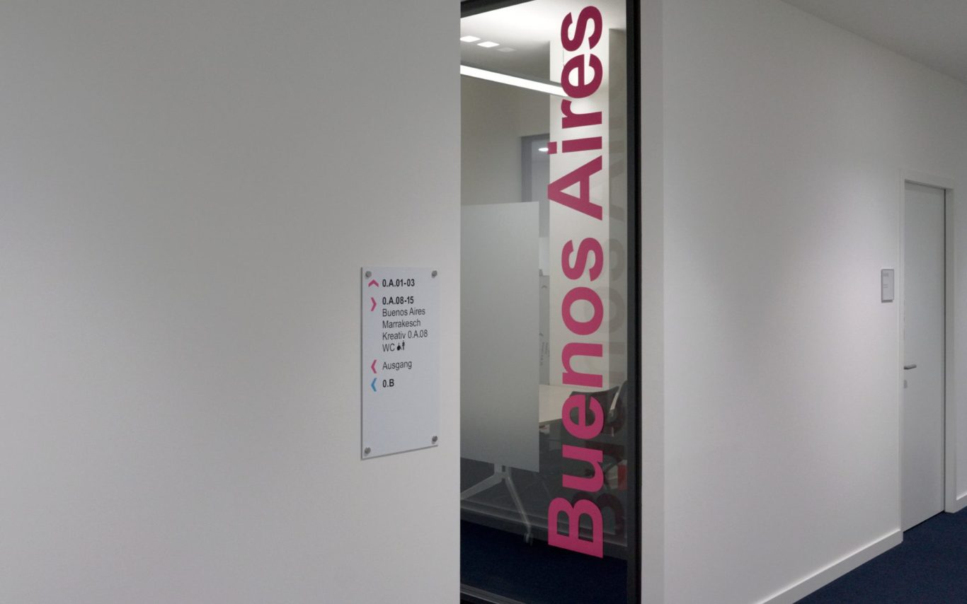 Glas-Besprechungsraum, beschriftet mit "Buenos Aires" in pink, neben einem Informationsschild.