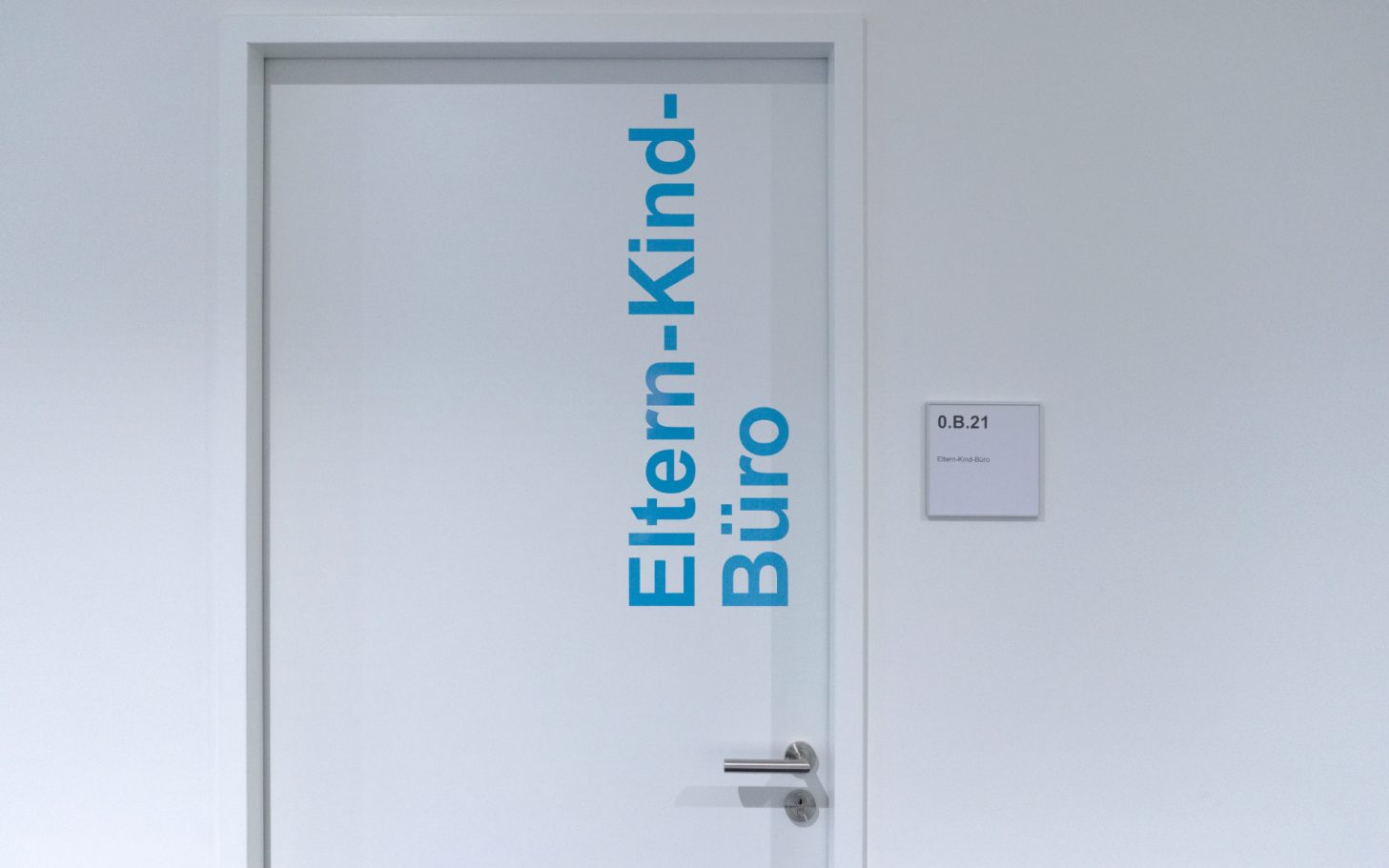 Tür des Eltern-Kind-Büros mit blauem Schriftzug auf weißem Hintergrund.