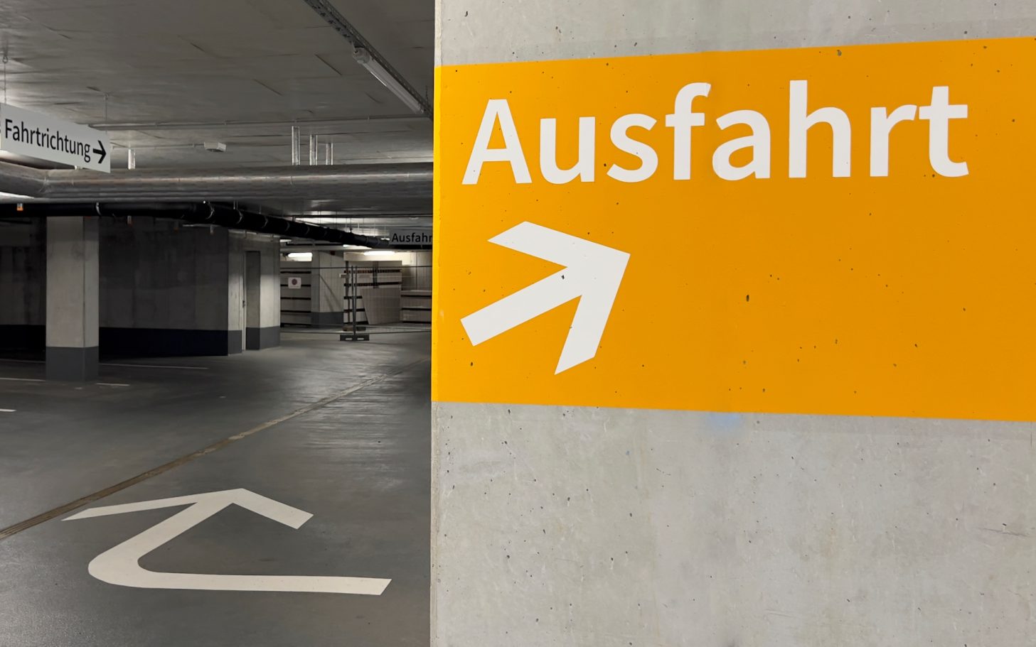 Parkgaragenfahrbahn mit gelben Wandstreifen und einem Pfeil nach rechts.