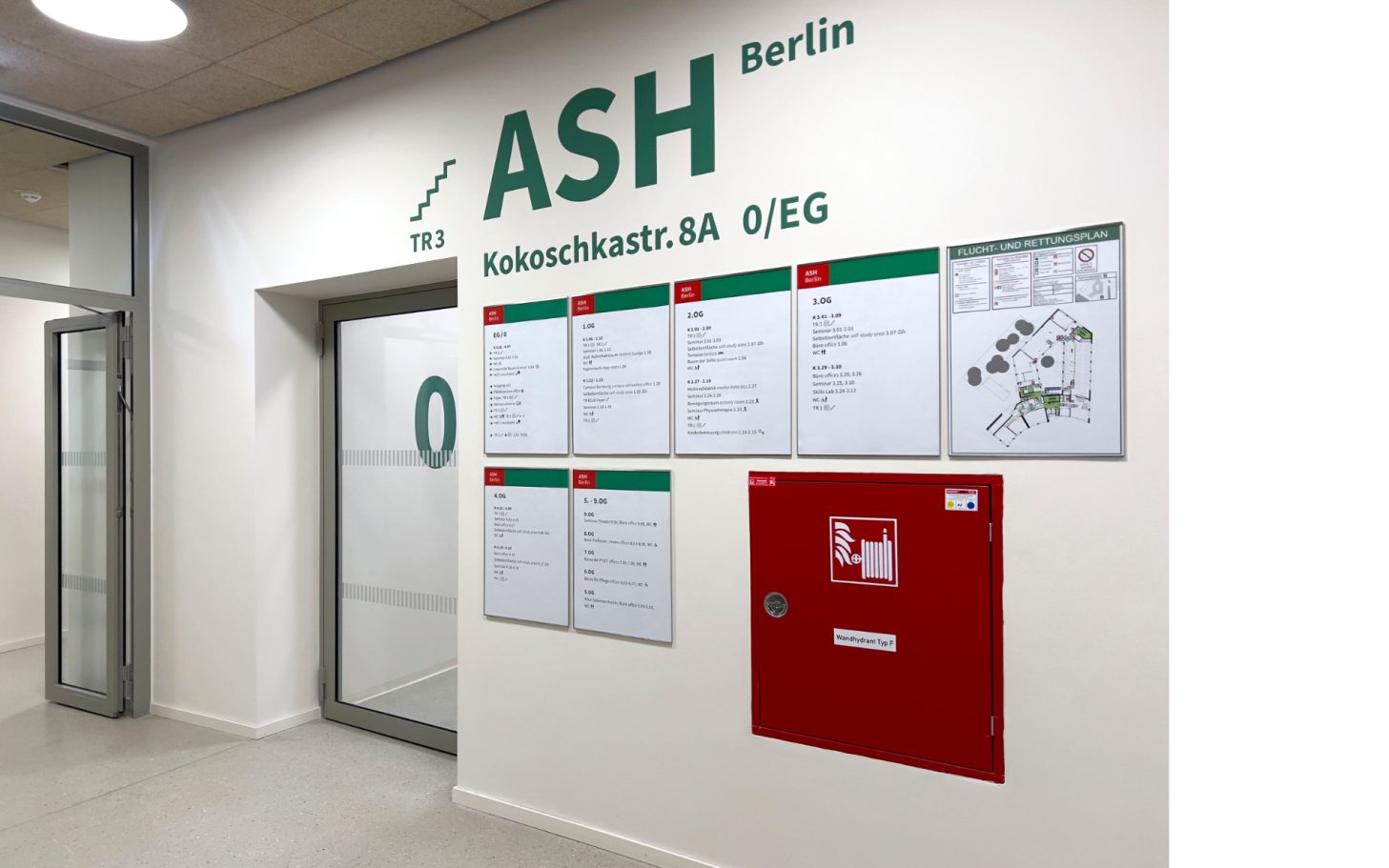 Wand mit Informationen der ASH Berlin, einschließlich Notfallhinweisen und Plänen.