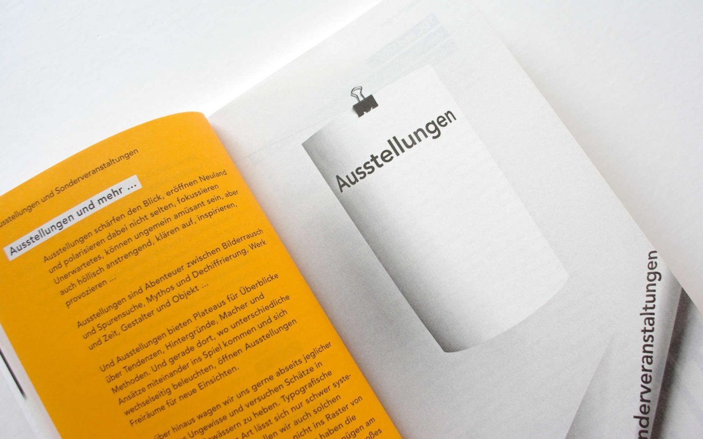 Ein offenes Buch mit orangefarbener Seite und einer weißen Seite mit Text im Schwarz-Weiß Foto.