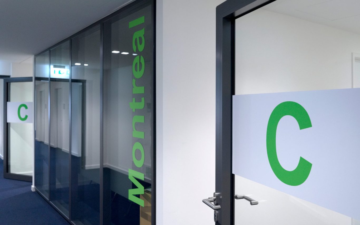 Glaswand, beschriftet mit "Montreal" und grünem "C" auf Glastüren.