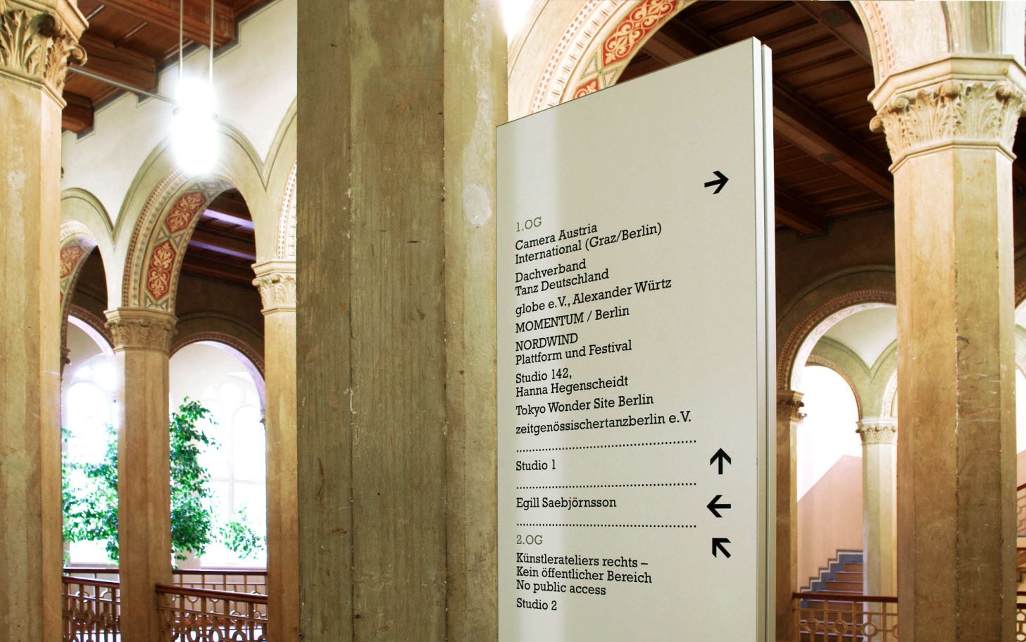 Helle Informationsstele in einem historischen Gebäude mit Wegweisern.